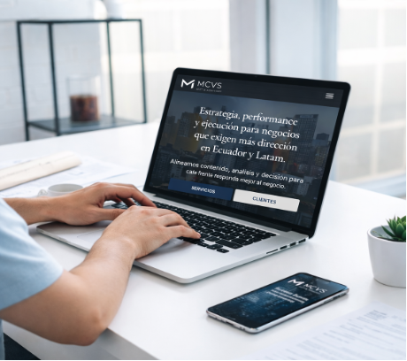Persona trabajando con laptop y smartphone mostrando el sitio MCVS, escritorio claro y entorno profesional